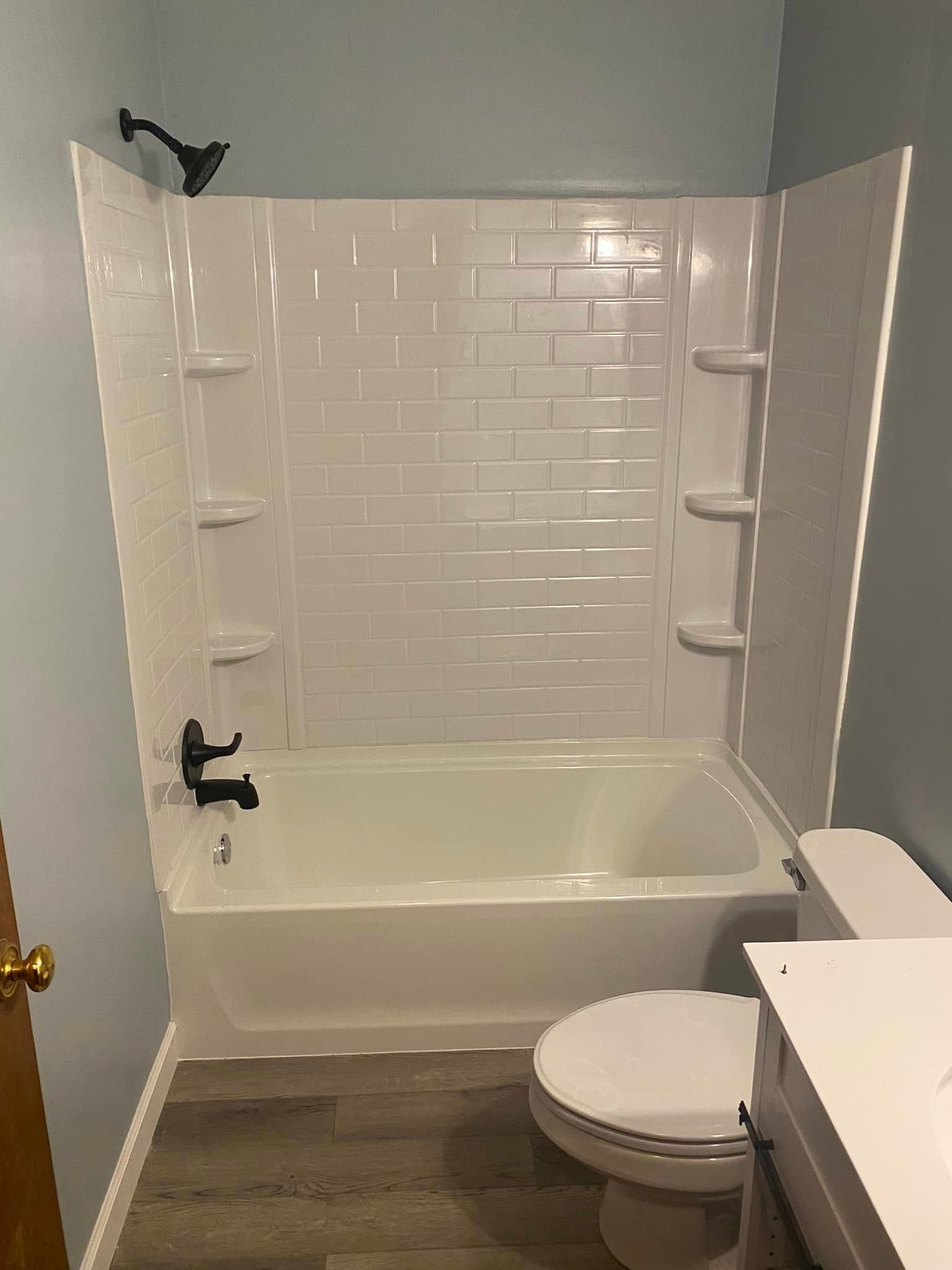 A bathroom featuring a white bathtub, a tiled surround with built-in shelves, matte black fixtures, and gray flooring.