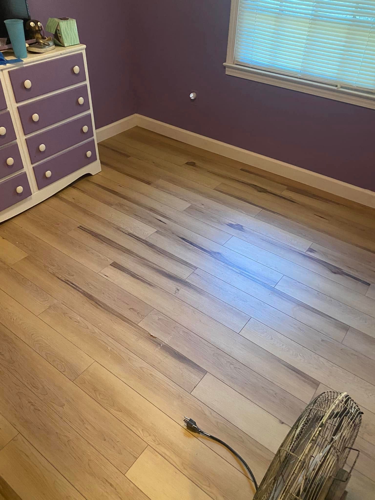 A light wood plank floor in a room with purple walls and a purple dresser.