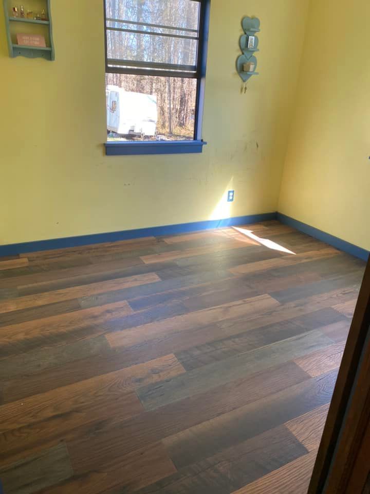 A room with yellow walls, dark wood-look plank flooring, a window, and wall-mounted decor.