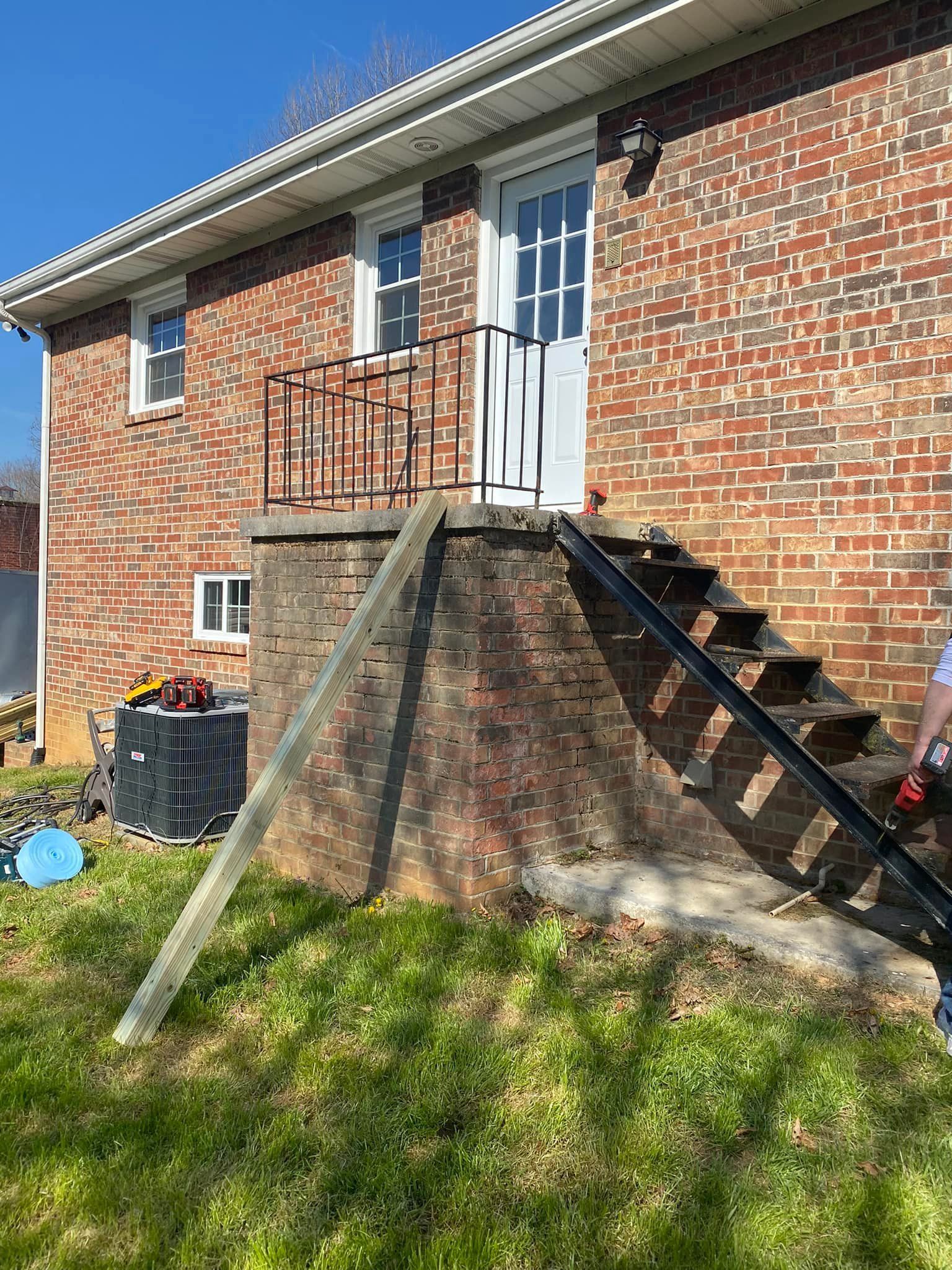 A brick house with a raised porch and stairs featuring new black metal railings, with construction gear on the lawn.