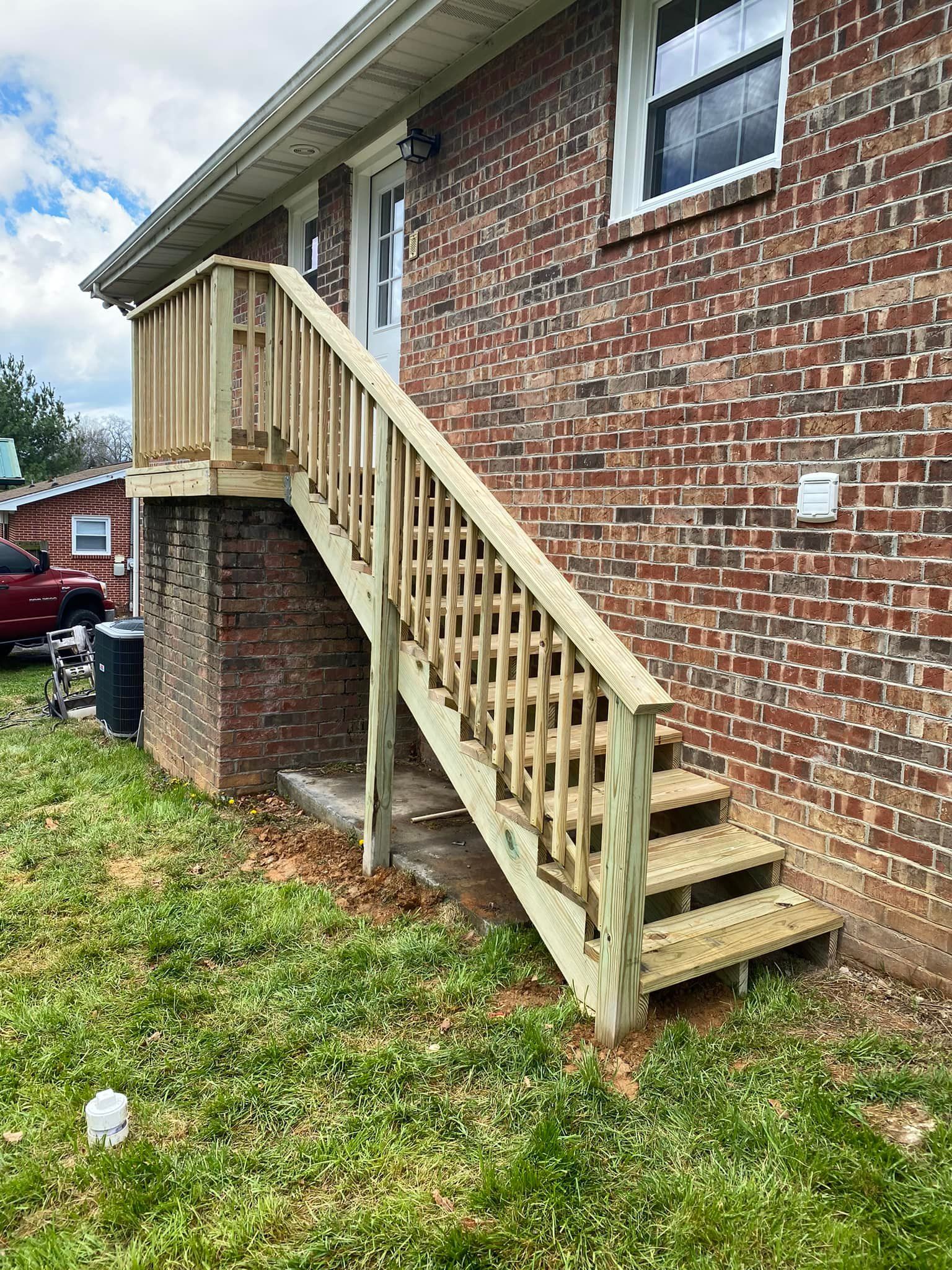 A newly built wooden staircase with railings attached to the brick exterior of a house.