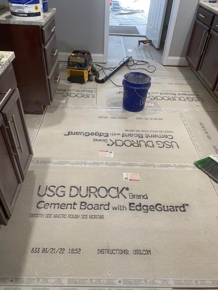 A kitchen floor under renovation, with USG Durock cement boards installed between dark wood cabinets and a tool bucket.