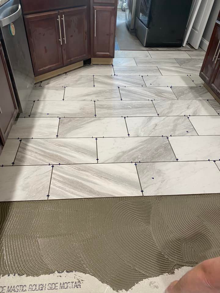 A partially tiled kitchen floor with a pattern of rectangular, white and grey marble-style tiles on thin-set mortar.