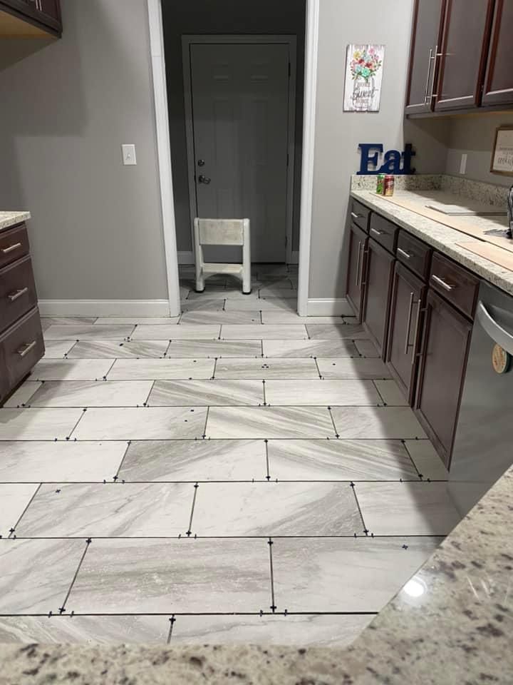 A kitchen with wood-look tile flooring in a running bond pattern, dark cabinets, granite countertops, and a white stool.