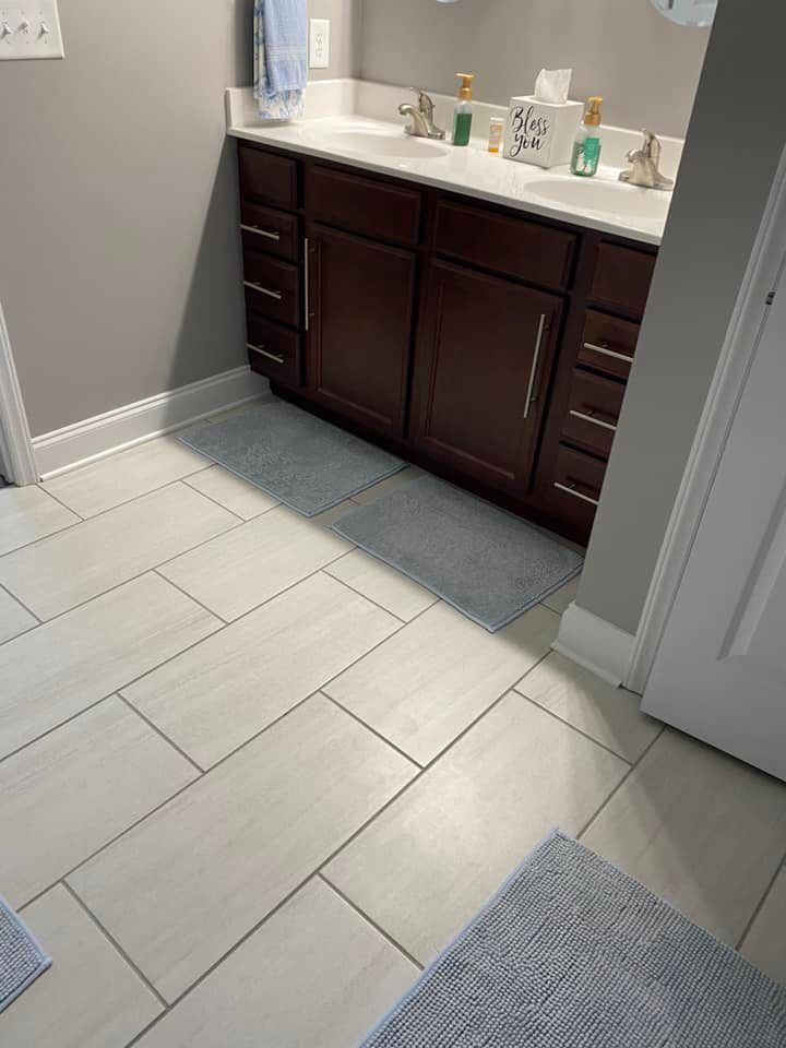 A modern bathroom vanity with a dark wood cabinet, white countertop, double sinks, and light-colored tiled flooring.