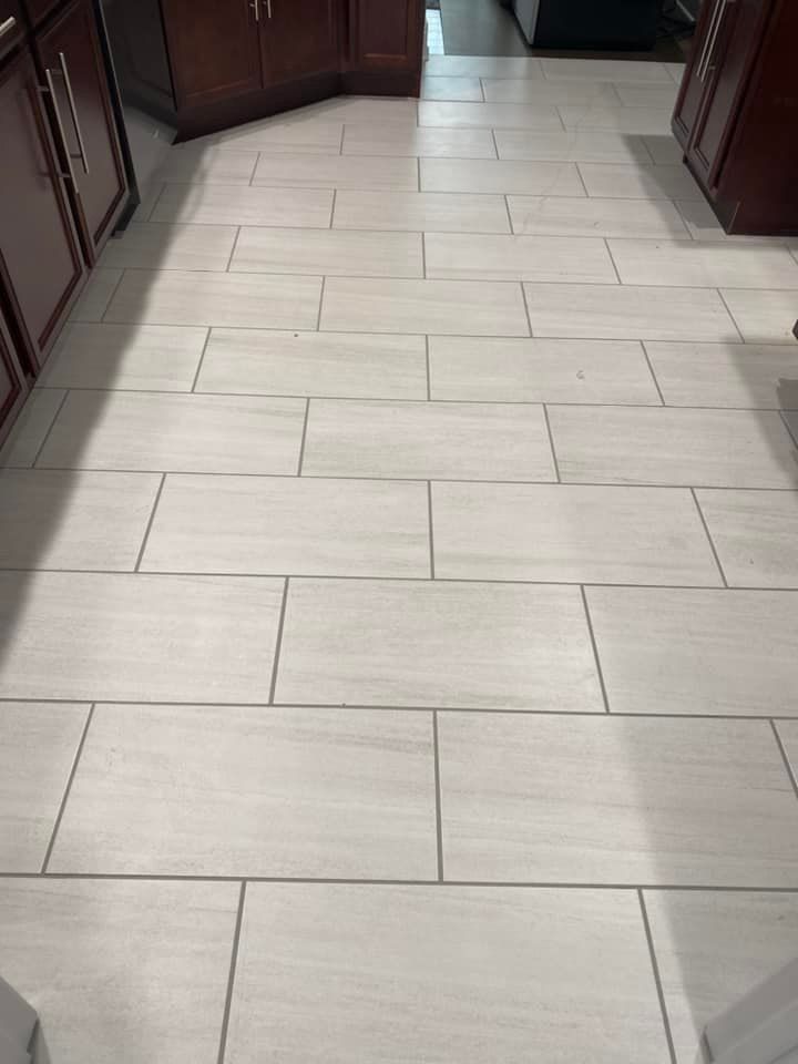 A light gray, wood-look tiled floor installed in a running bond pattern between dark wood kitchen cabinets.