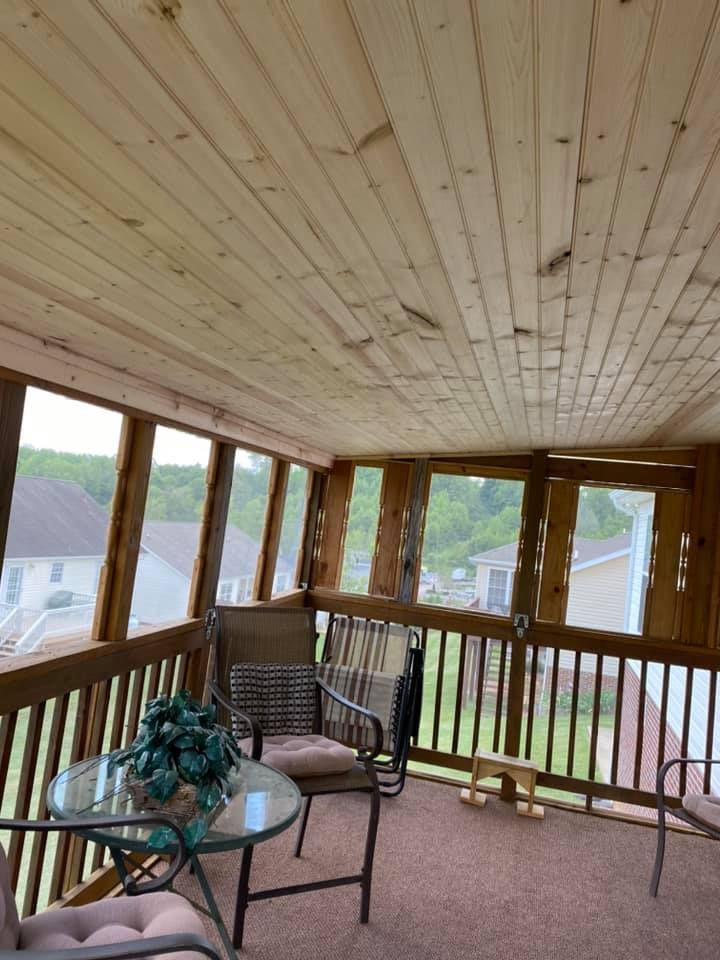 A screened-in porch with wood-paneled ceiling, patio furniture, and a view of neighboring houses and trees.