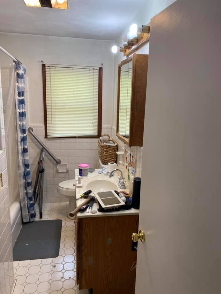 A before image of the bathroom with a white vanity, a mirror, a toilet, a shower with a blue and white curtain,