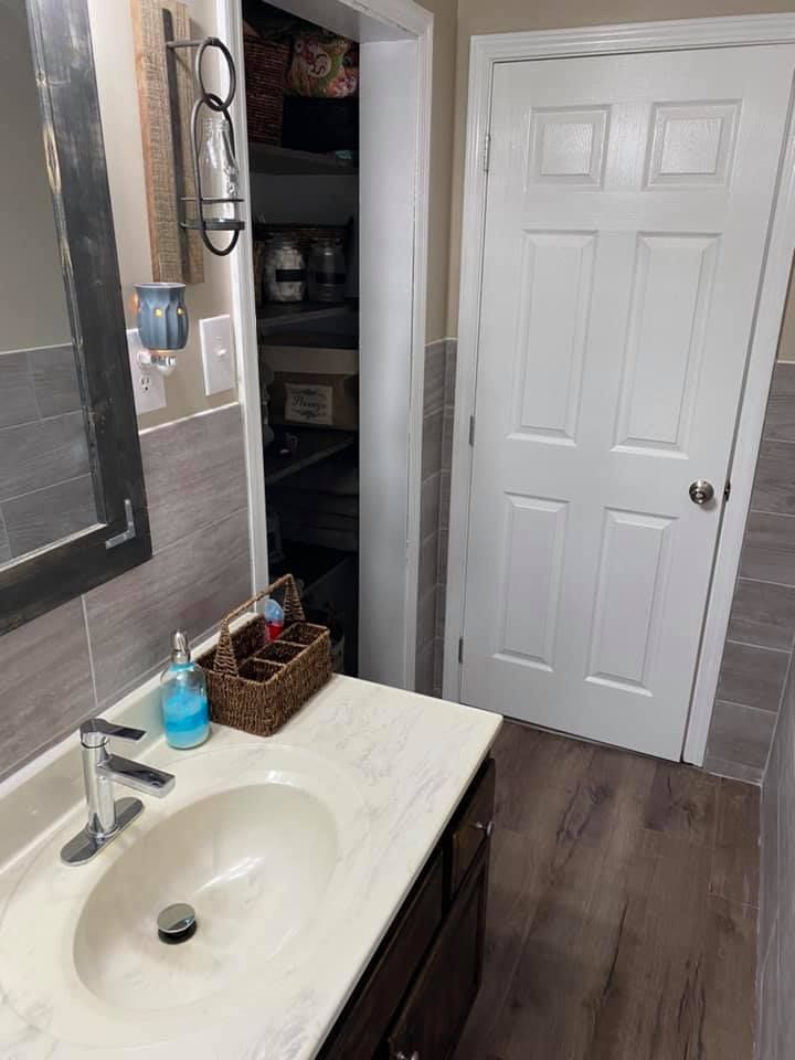 A bathroom vanity with a white sink and faucet, next to an open doorway revealing a closet, and a white six-panel door.