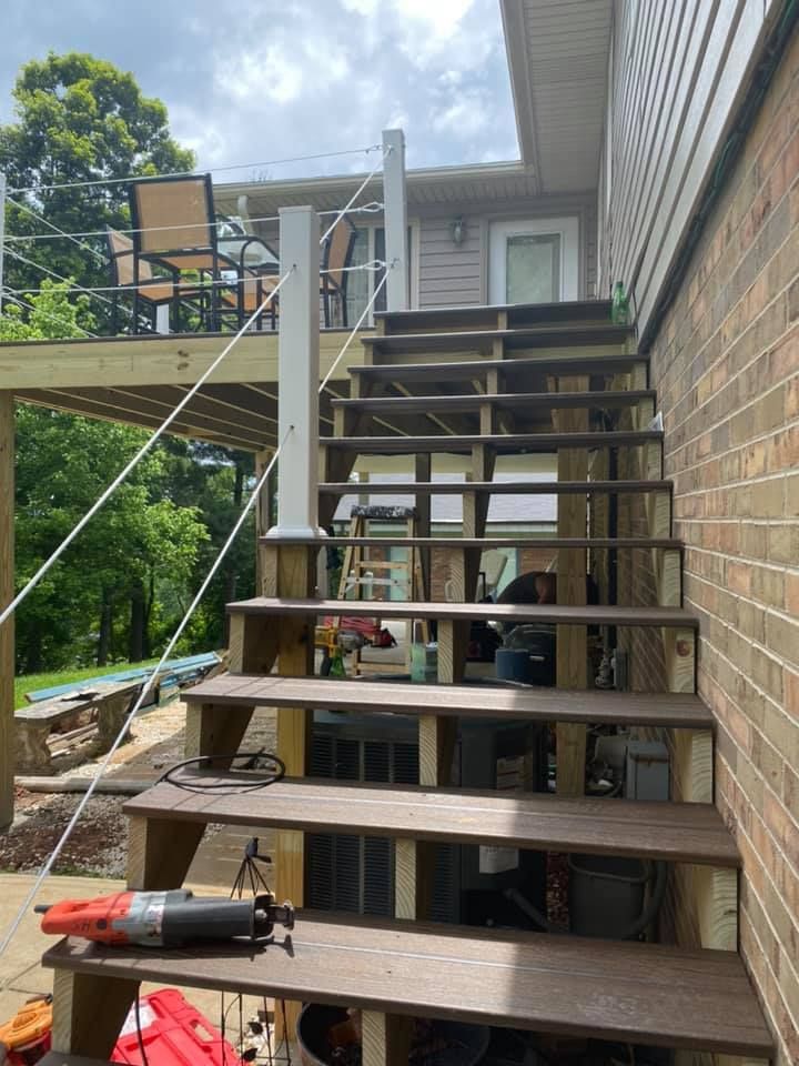 Newly installed wooden stairs leading up to an elevated deck with metal cable railings, viewed from the bottom.