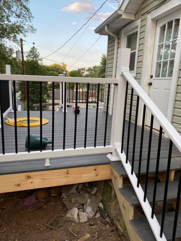 A newly built wooden deck with white railings and black balusters leading to an exterior door of a house.