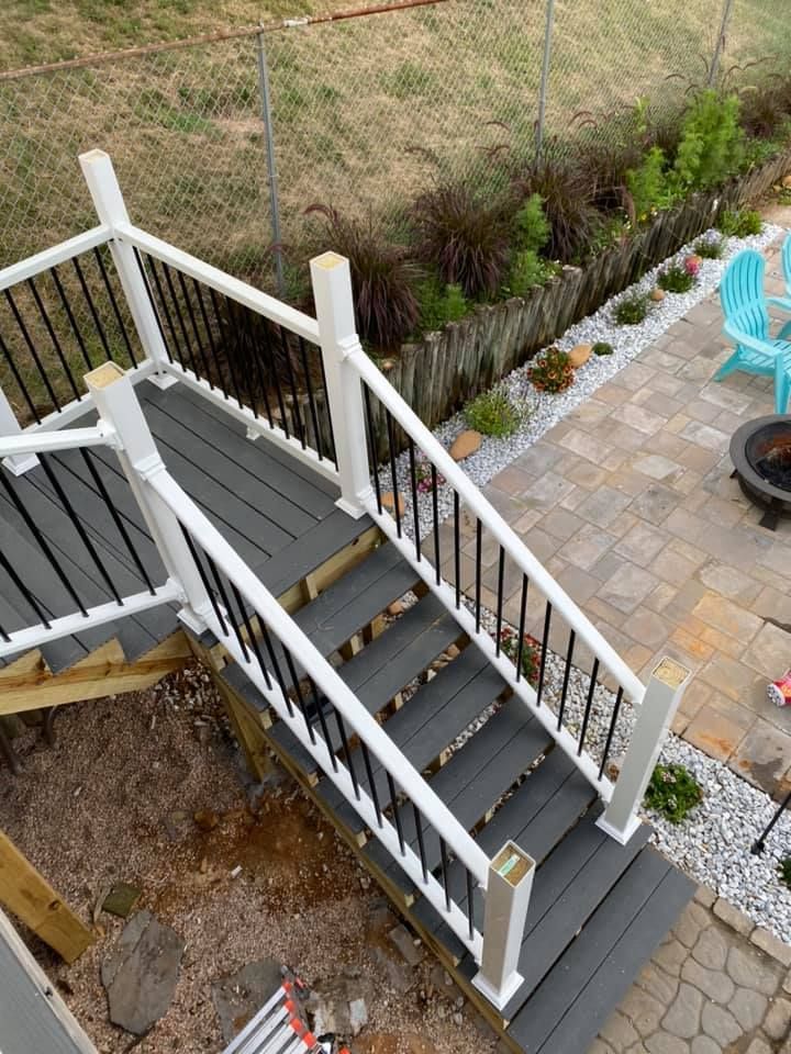 Gray deck stairs with white railings and black balusters descending to a stone patio with a fire pit.