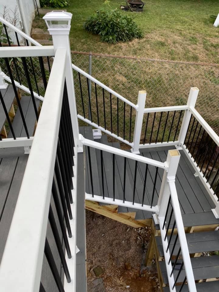 High-angle view of outdoor gray composite deck stairs with white railings and black balusters leading to a grassy yard.