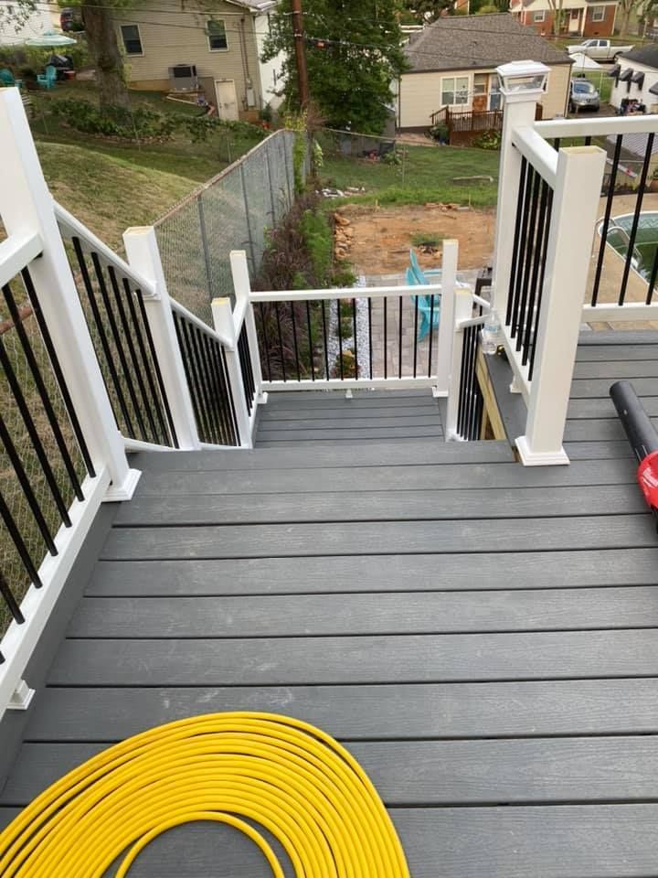 A view down gray deck stairs with white railings, looking toward a fenced backyard, patio, and neighboring houses.