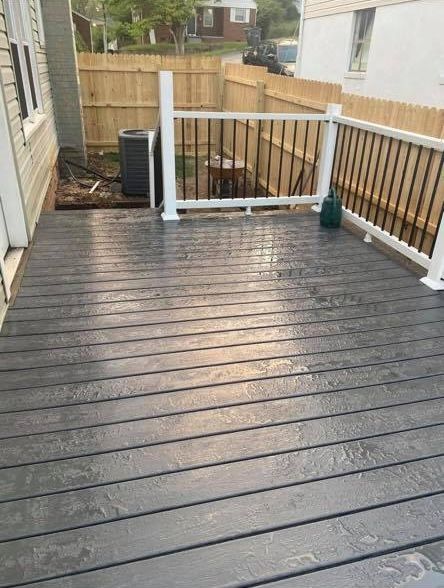 A gray wooden deck with white railing, viewed from a doorway, overlooking a fenced backyard with an air conditioning unit.