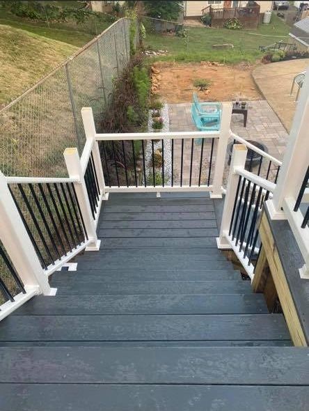 A high-angle view looking down dark grey outdoor stairs with white railings and black balusters toward a backyard patio.