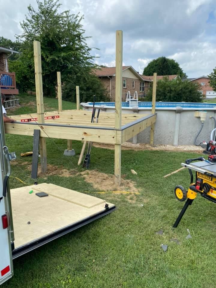 A wooden deck frame under construction in a backyard next to an above-ground swimming pool, with tools visible nearby.