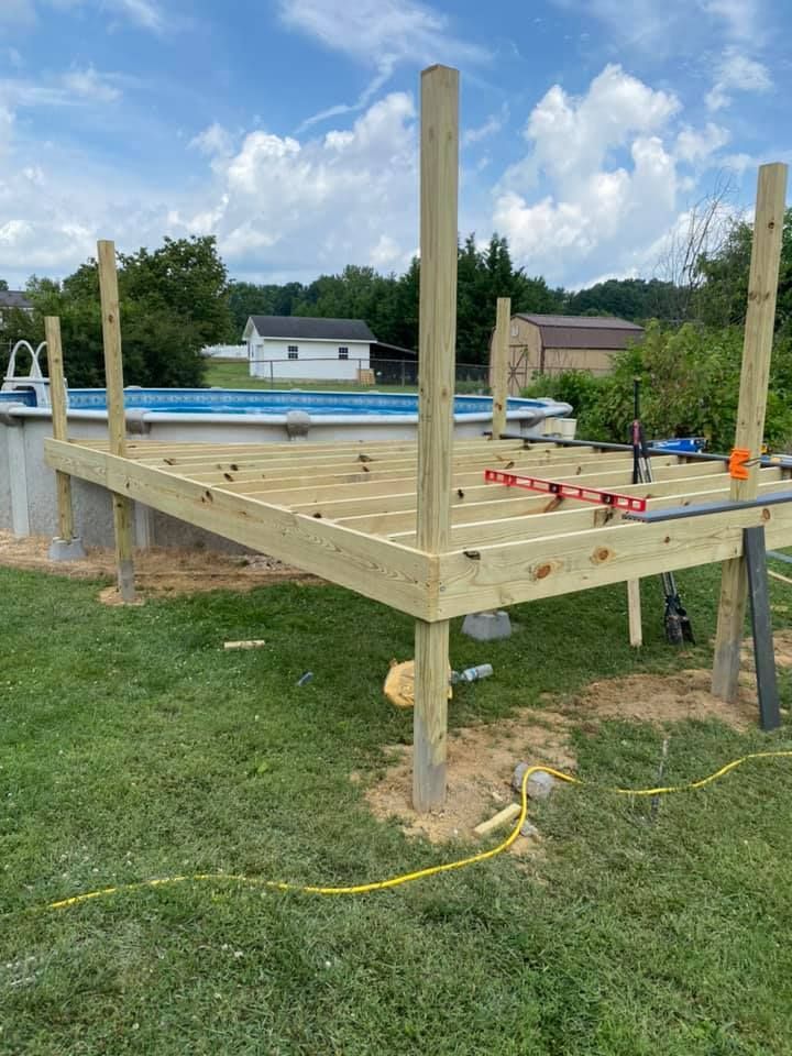 A wooden deck frame under construction in a backyard, featuring vertical support posts and an above-ground pool nearby.
