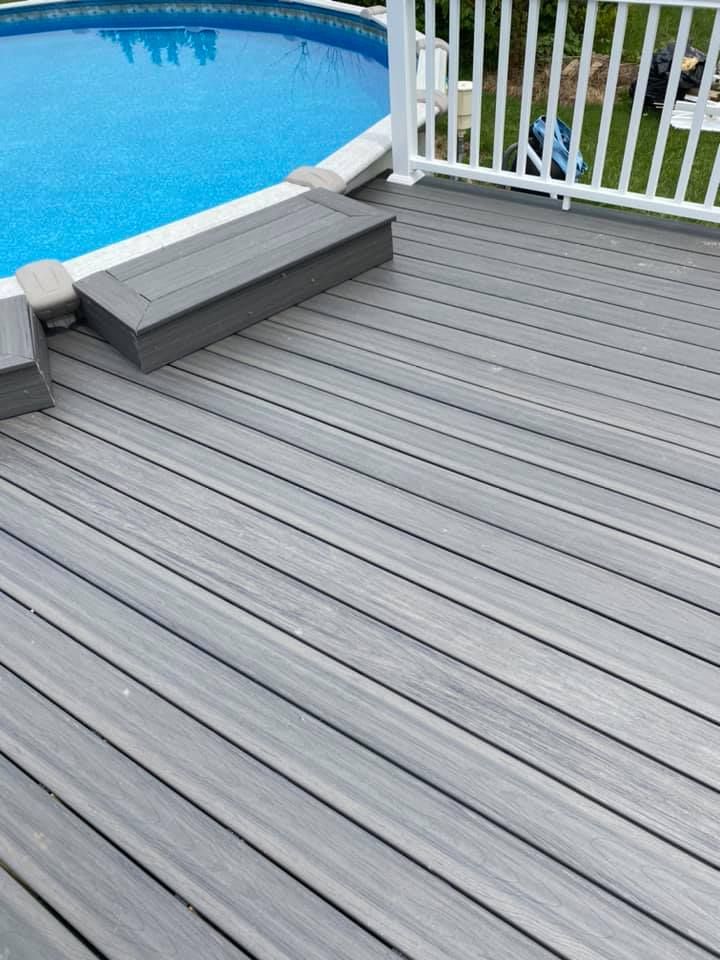 A gray composite deck with a small step leading to an above-ground swimming pool and white railing.