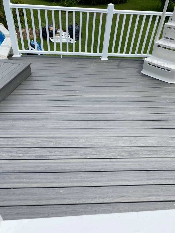 A gray composite deck with white railings and pool steps, overlooking a lawn.