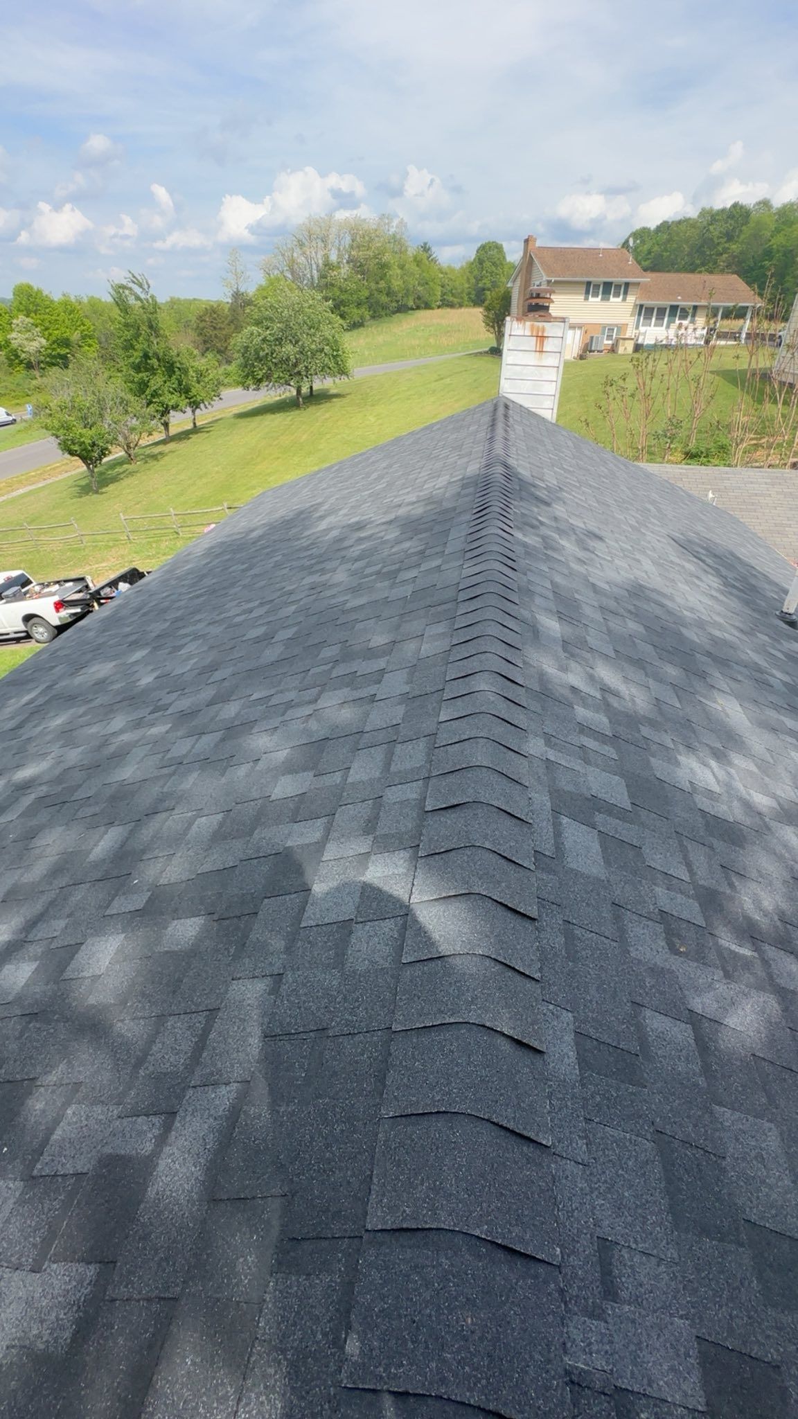 An after image of a high-angle view of a grey shingled roof with a prominent ridge vent, overlooking a green yard