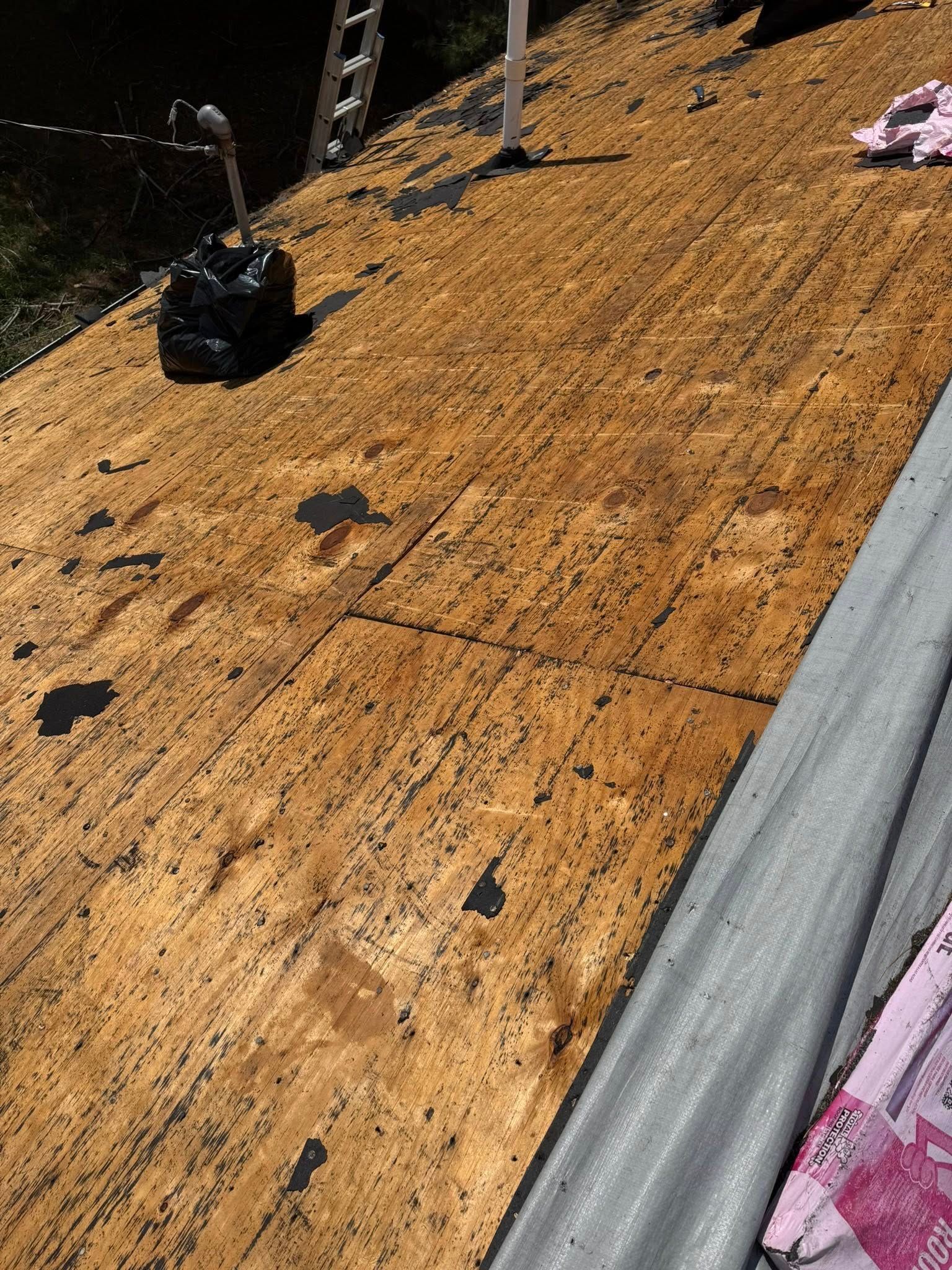 A high-angle view of a wooden roof deck under construction with a roll of roofing underlayment on the right.