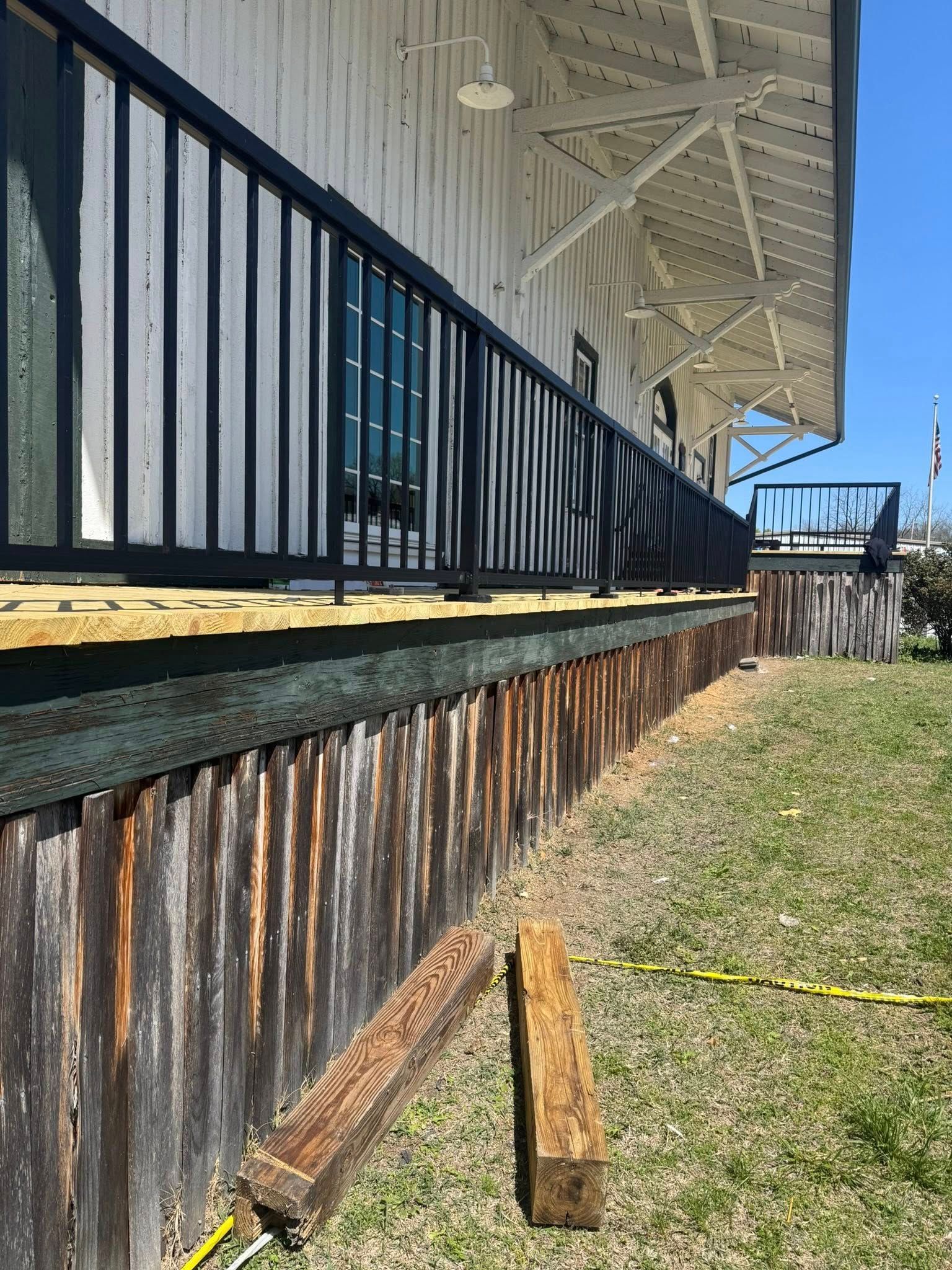 A low-angle view of a white building exterior with a deck, black railings, weathered wood skirting, and two wood beams.
