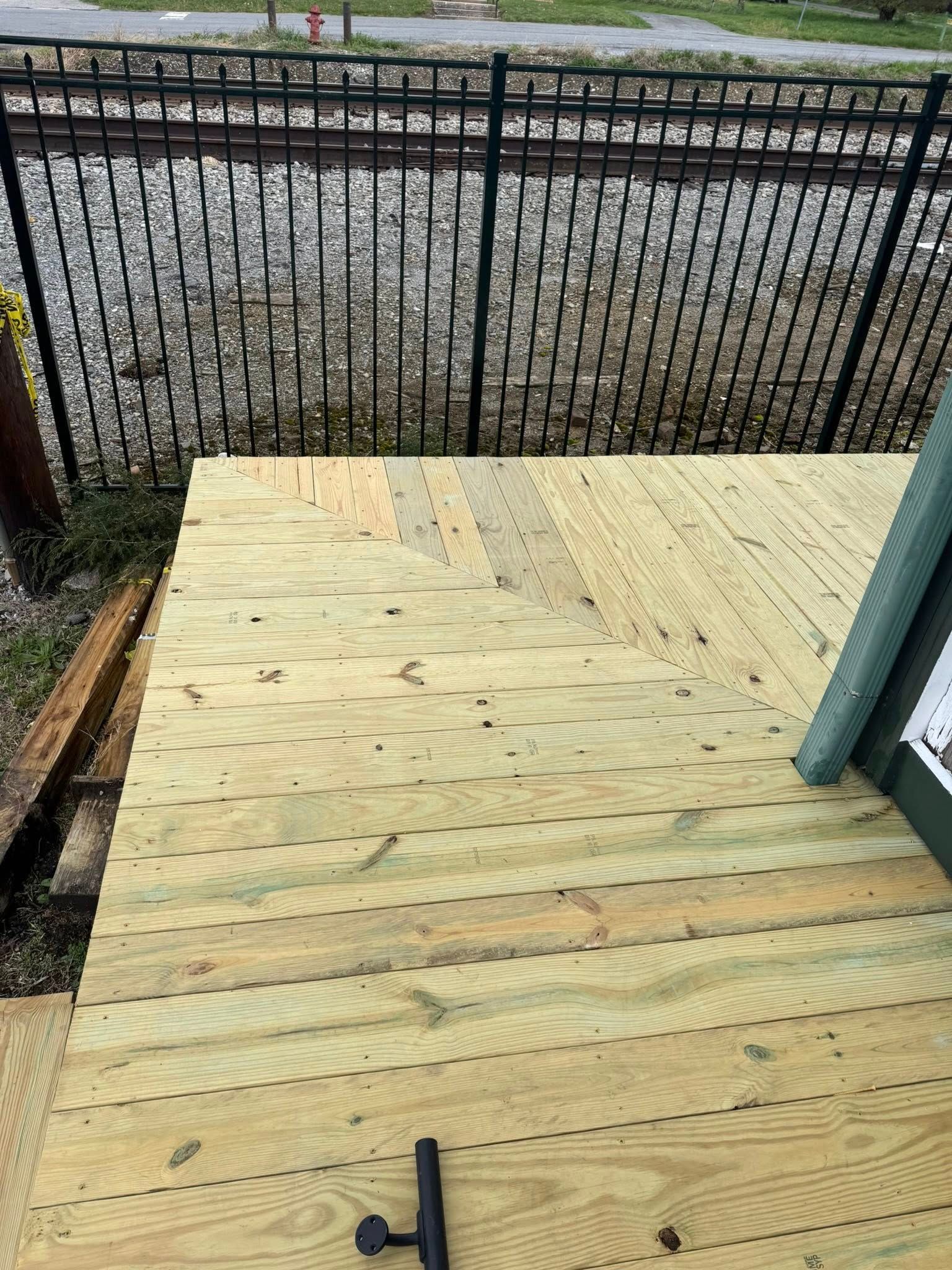 Newly installed light-colored wooden deck boards with a diagonal pattern transition, bordered by a black metal fence.