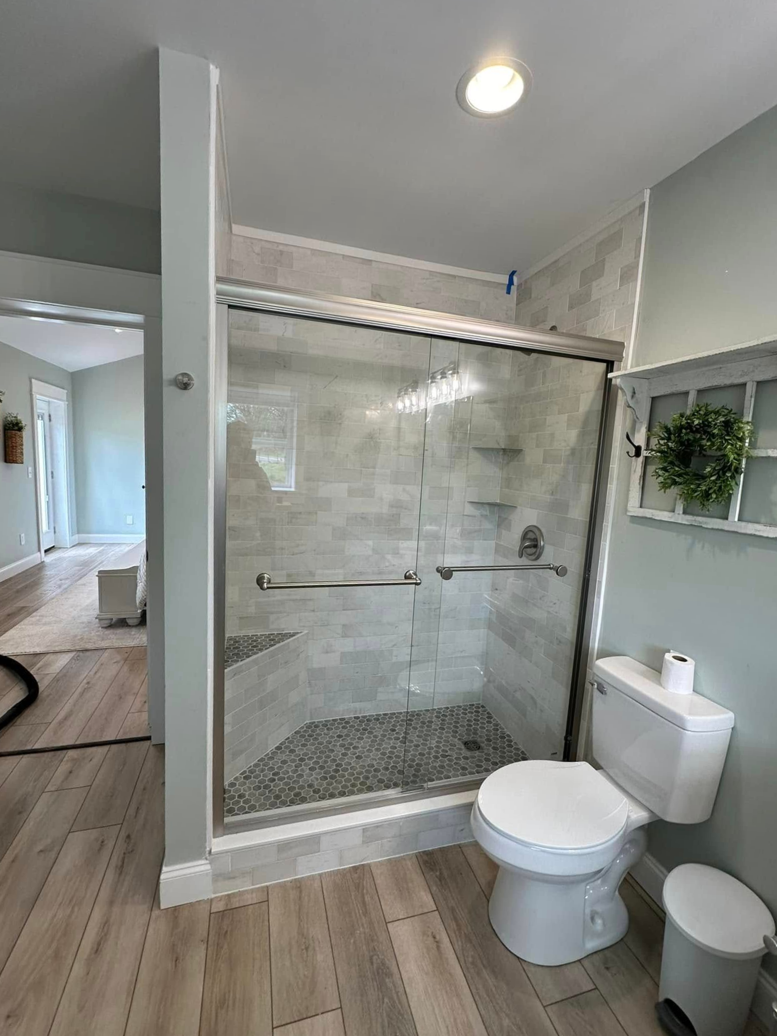 A bathroom features a walk-in shower with stone tile, a glass door, and a white toilet next to it on light wood flooring.