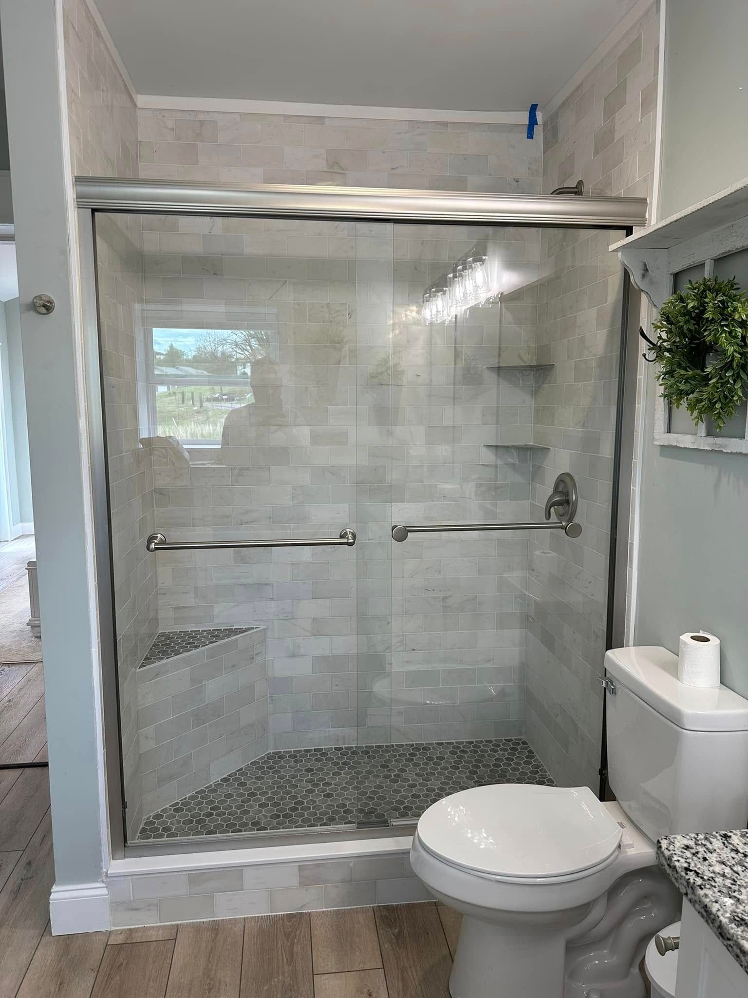 A modern bathroom featuring a tiled walk-in shower with a glass door, built-in seat, and a toilet beside it.