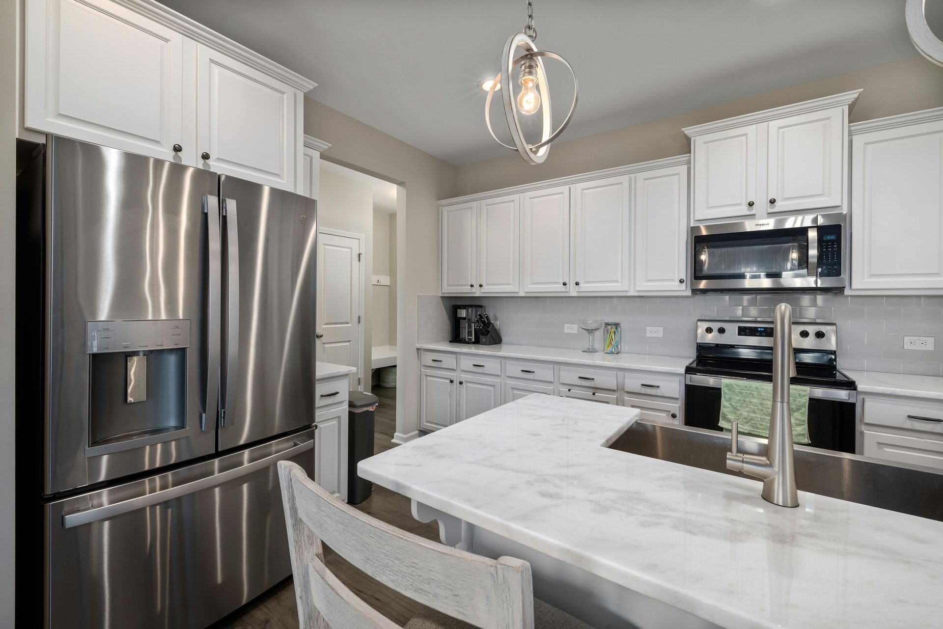 A modern kitchen featuring white cabinets, stainless steel appliances, a marble-topped island, and a geometric pendant light.