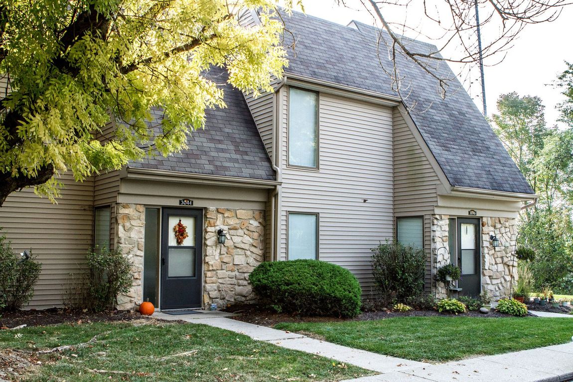Two-story townhouses with light siding and stone accents; a tree and shrubs in the front yard.