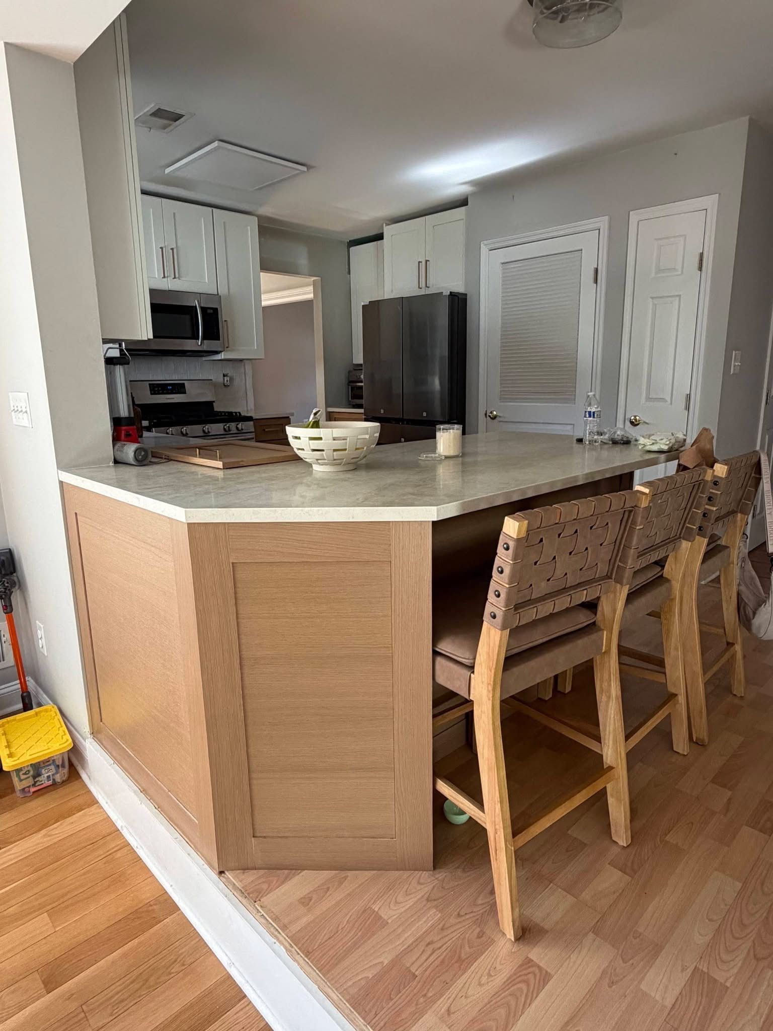 Kitchen with a curved island, wood stools, light cabinets, and stainless steel refrigerator.