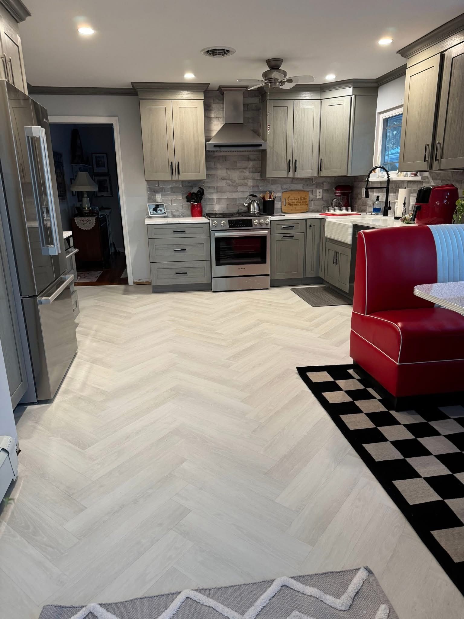 Modern kitchen with gray cabinets, white herringbone floor, and a red chair on a black rug
