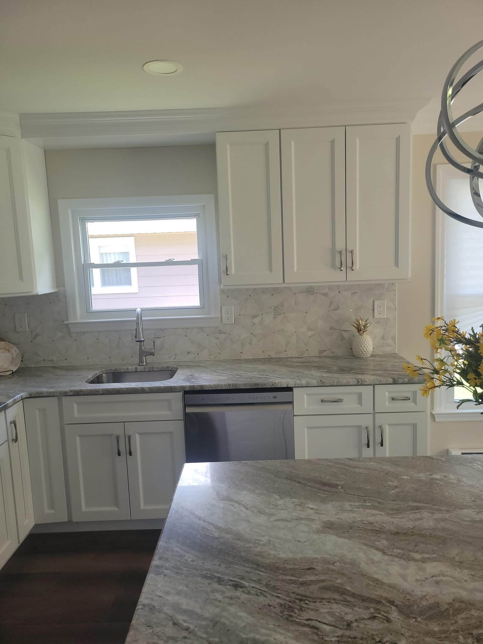 Bright white kitchen with marble countertops, window over the sink, and dark wood floor