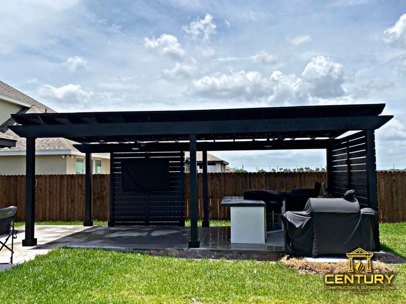 A backyard with a black pergola and a grill.