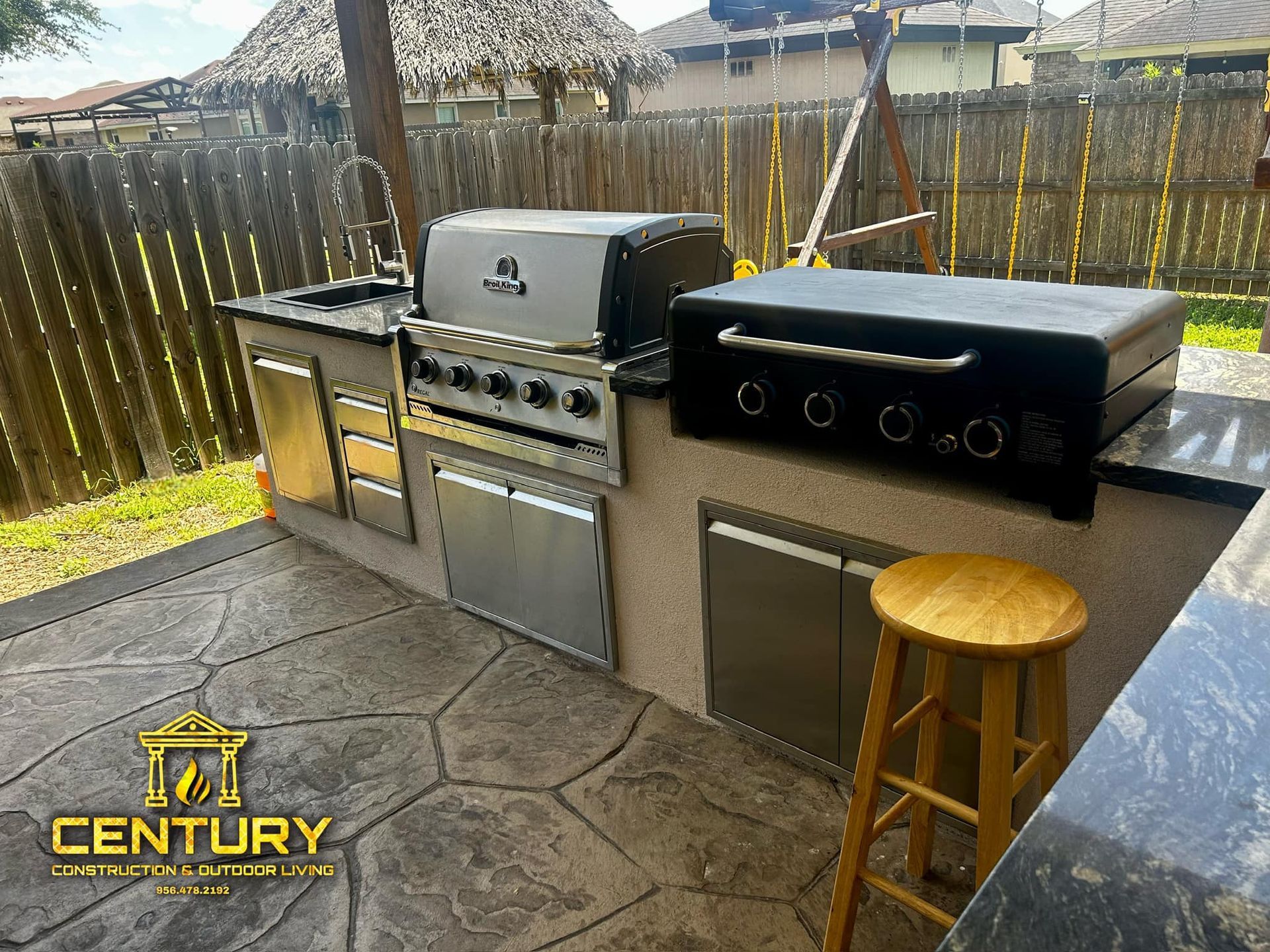 An outdoor kitchen with a grill , sink , and stools.