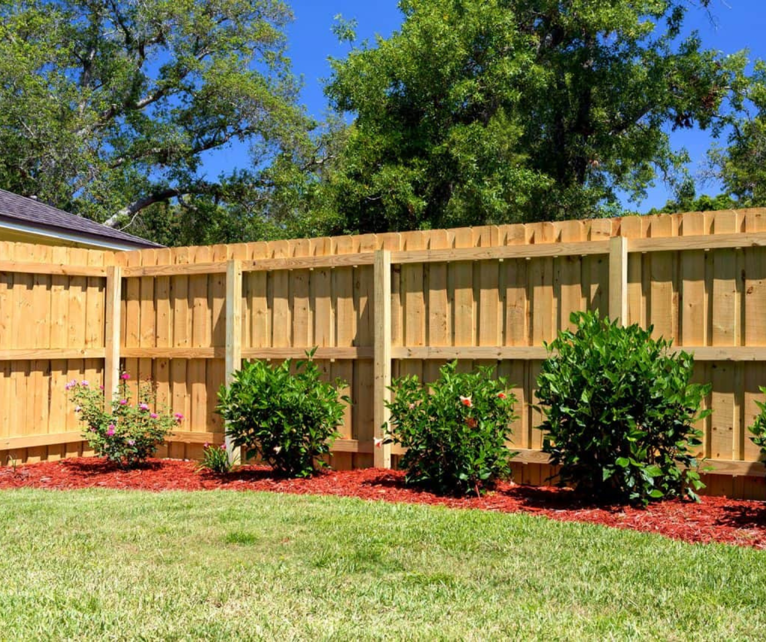 A wooden fence surrounds a lush green lawn in a backyard.