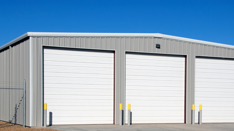 A metal building with three white garage doors against a blue sky.