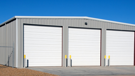 A metal building with three white garage doors and a blue sky in the background.