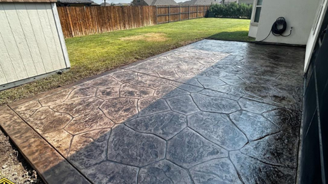 A concrete patio with a shed in the background and a fence in the backyard.