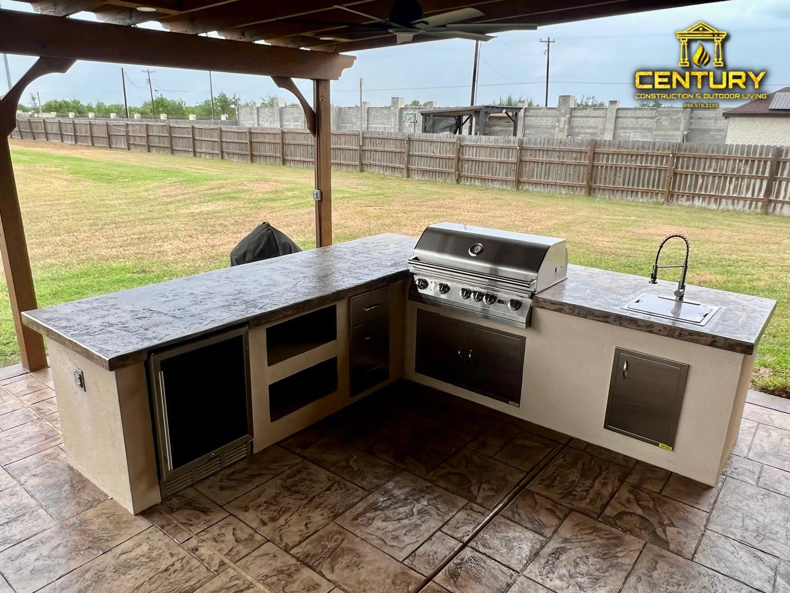 A large outdoor kitchen with a grill and sink under a pergola.