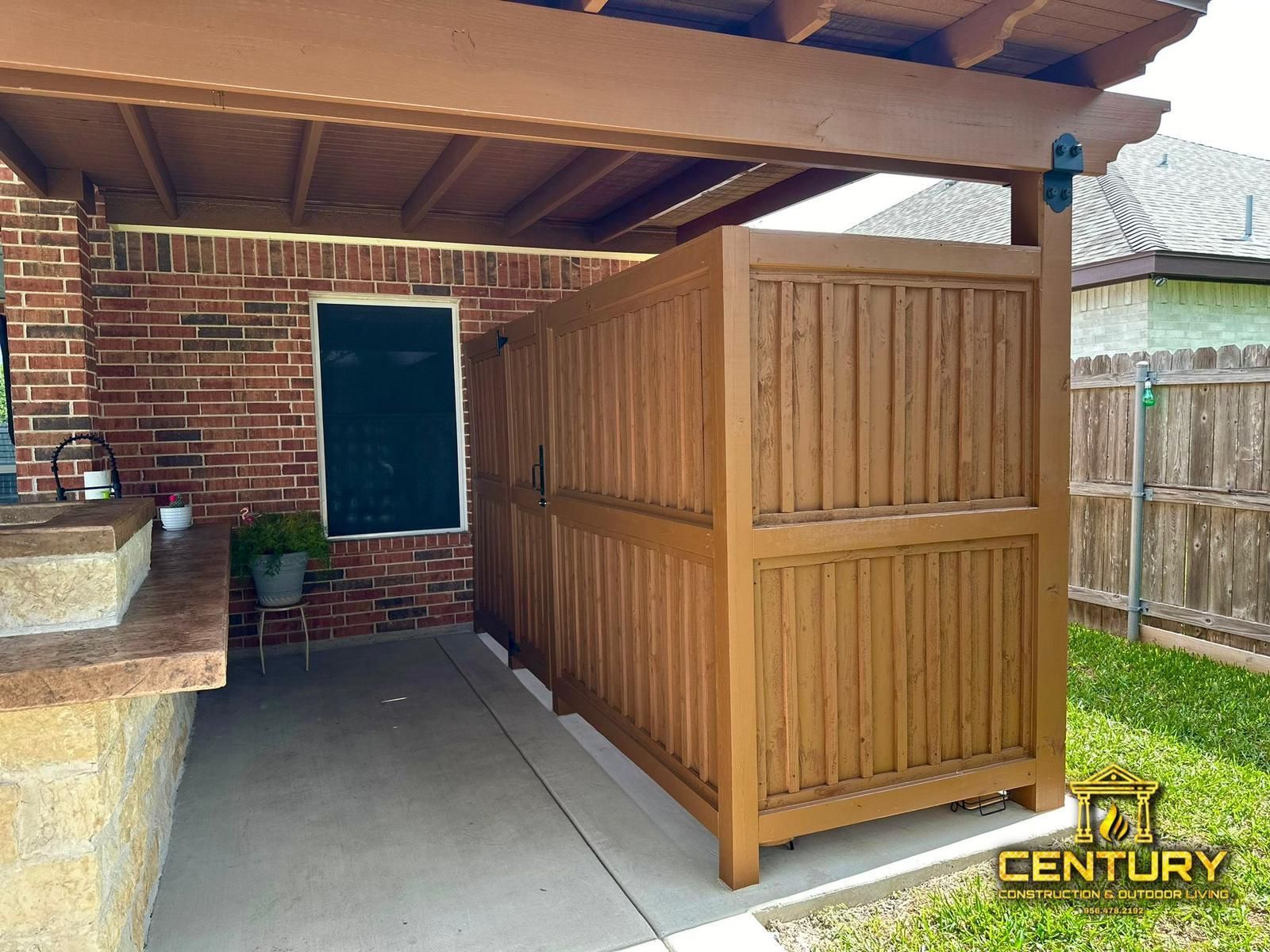 A wooden fence is sitting under a pergola in a backyard.