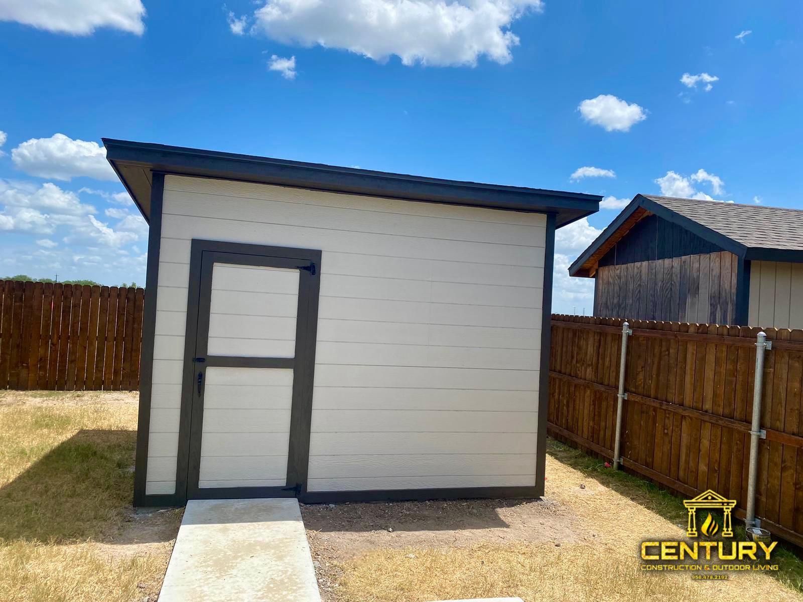 A small white shed with a door in the backyard next to a wooden fence.