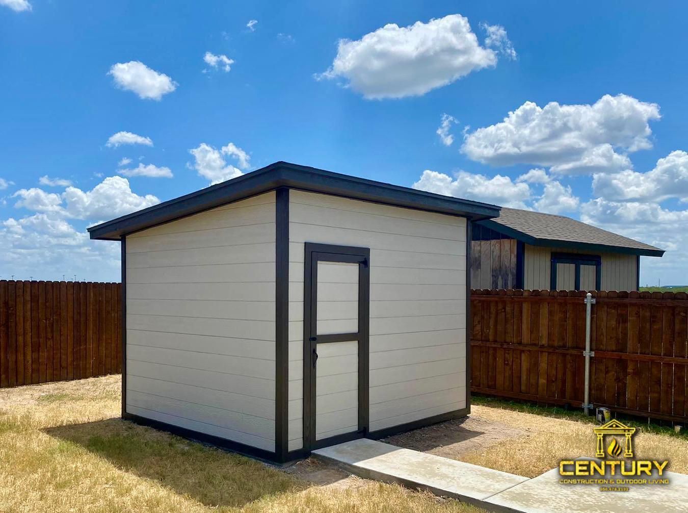 A small white shed is in the backyard of a house.