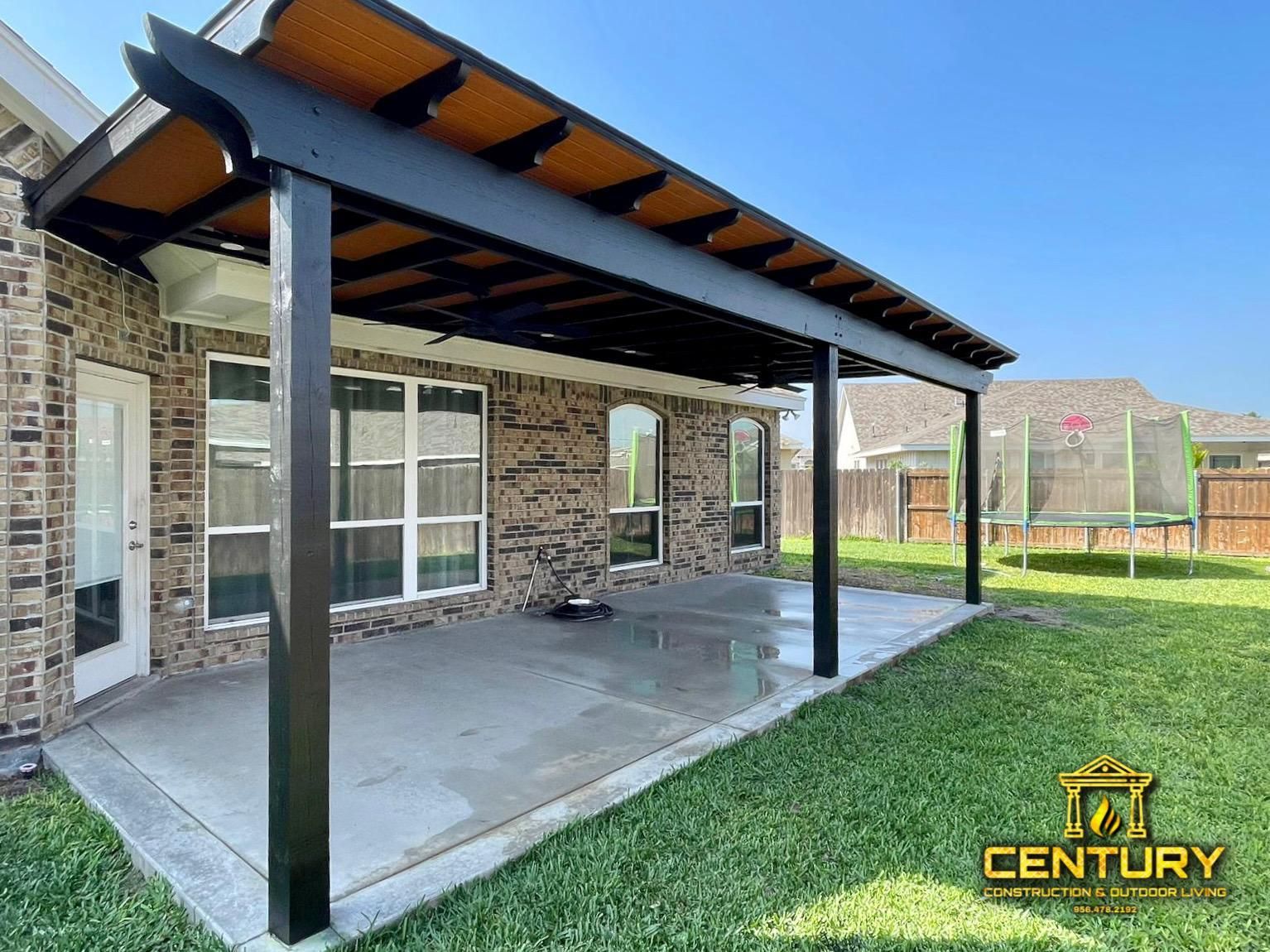 A patio with a pergola and a trampoline in the backyard of a house.