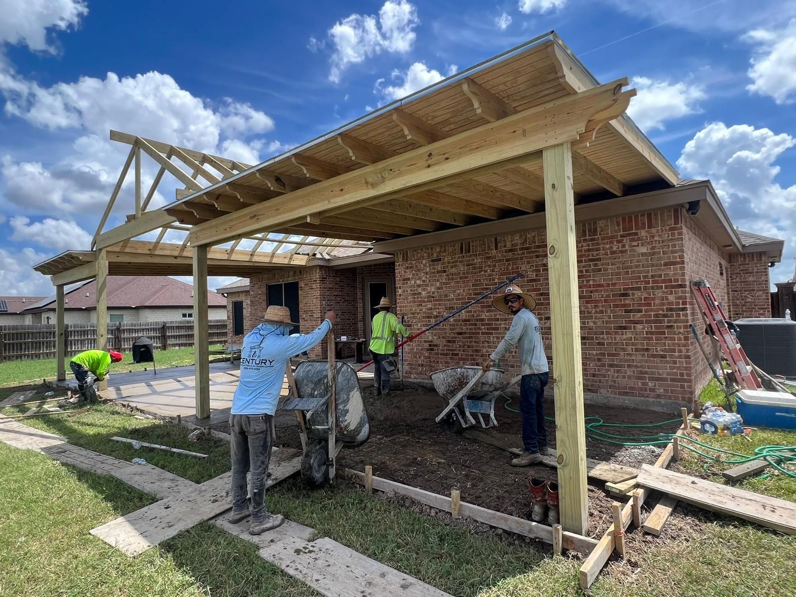 A group of men are working on a wooden pergola in front of a brick house.