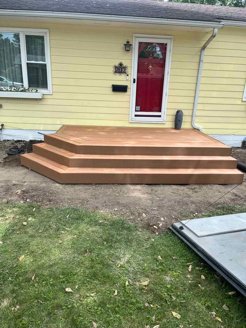 A yellow house with a wooden deck and stairs in front of it.