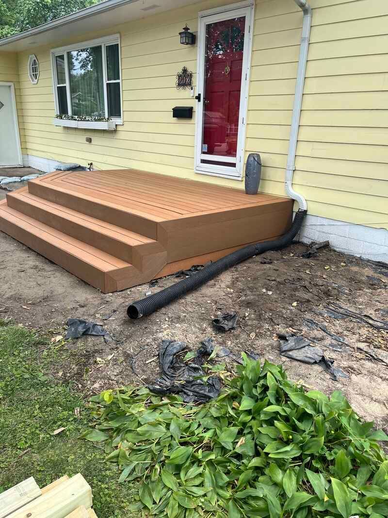 A yellow house with a wooden deck and stairs in front of it.