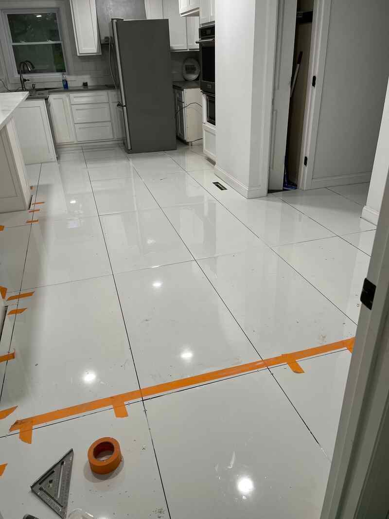 A kitchen with white tiles and orange tape on the floor.